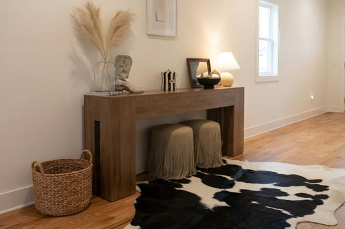 Cowhide rug in a large black and white spotted pattern lying beneath a wooden console table with an irregular natural shape.