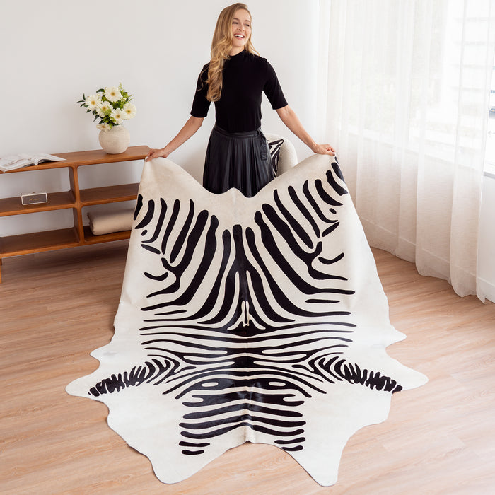 Woman holding a zebra cowhide rug in a room with a wooden floor and white curtains.