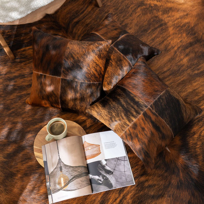 Brown cowhide rug with pillows and a magazine on a wooden surface