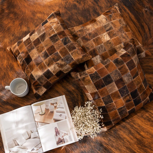 Brown checkered pillow on a textured surface with a magazine and flowers nearby