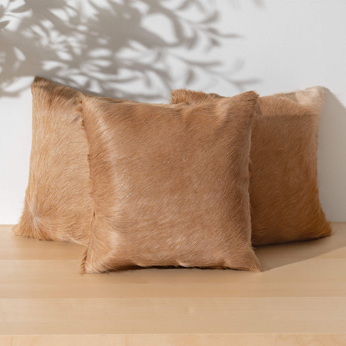 Three brown fur pillows on a wooden surface with a neutral background