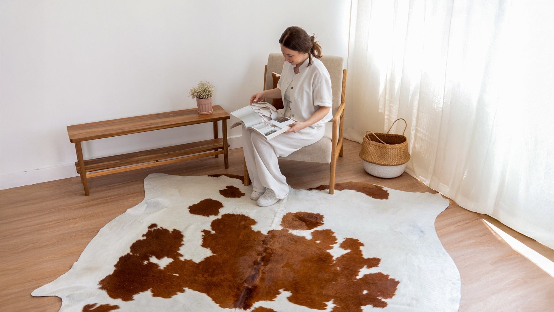 Woman sitting on an armchair, reading a magazine, with a large Brown and White Cowhide Rug on the floor.
