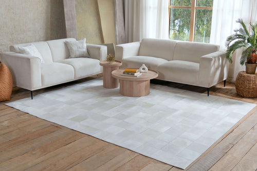 Cowhide large rectangular patchwork rug in solid off-white and cream squares styled in a modern living room with white sofas.