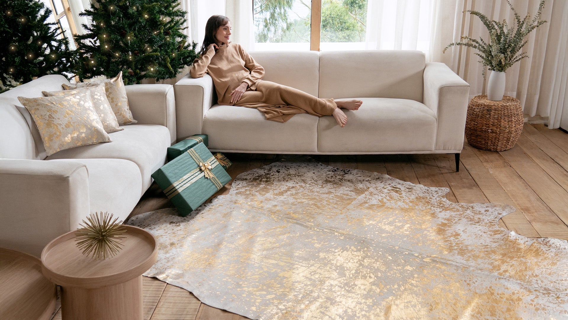 A woman relaxing on a white sofa next to a Metallic Gold on White Cowhide Rug in a bright holiday-themed room.