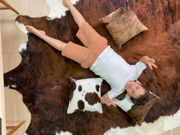 A young boy lying on his cowhide rug, barefoot and chilling.