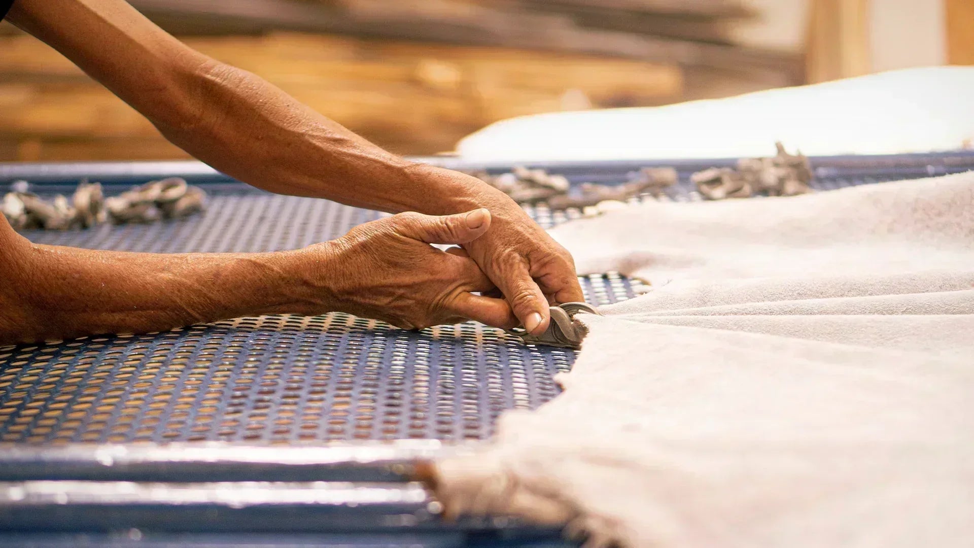 A detailed shot of an artisan's weathered hands using specialized tools to stretch and secure a hide onto a drying frame, highlighting the meticulous attention to detail in the tanning process.