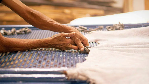 A detailed shot of an artisan's weathered hands using specialized tools to stretch and secure a hide onto a drying frame, highlighting the meticulous attention to detail in the tanning process.