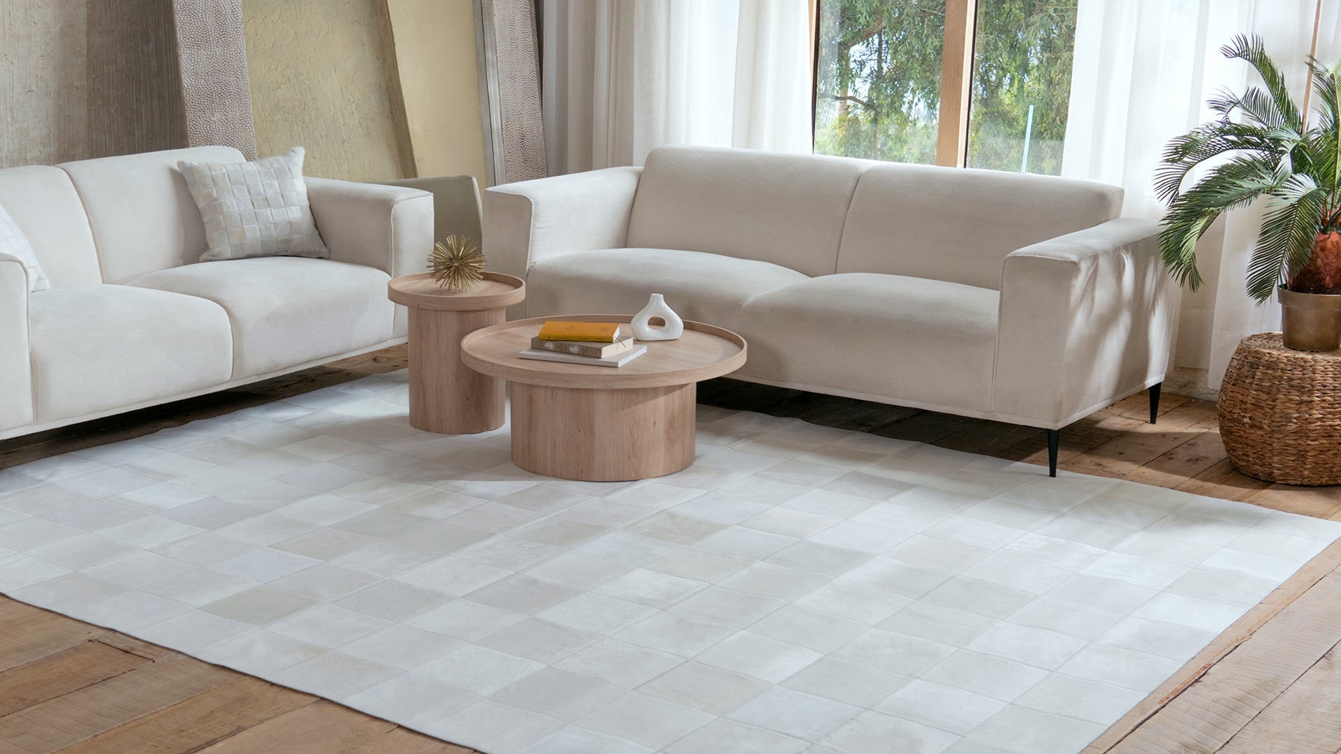 A living room with two white sofas and a Rhodes White Patchwork Cowhide Rug on a rustic wood floor.