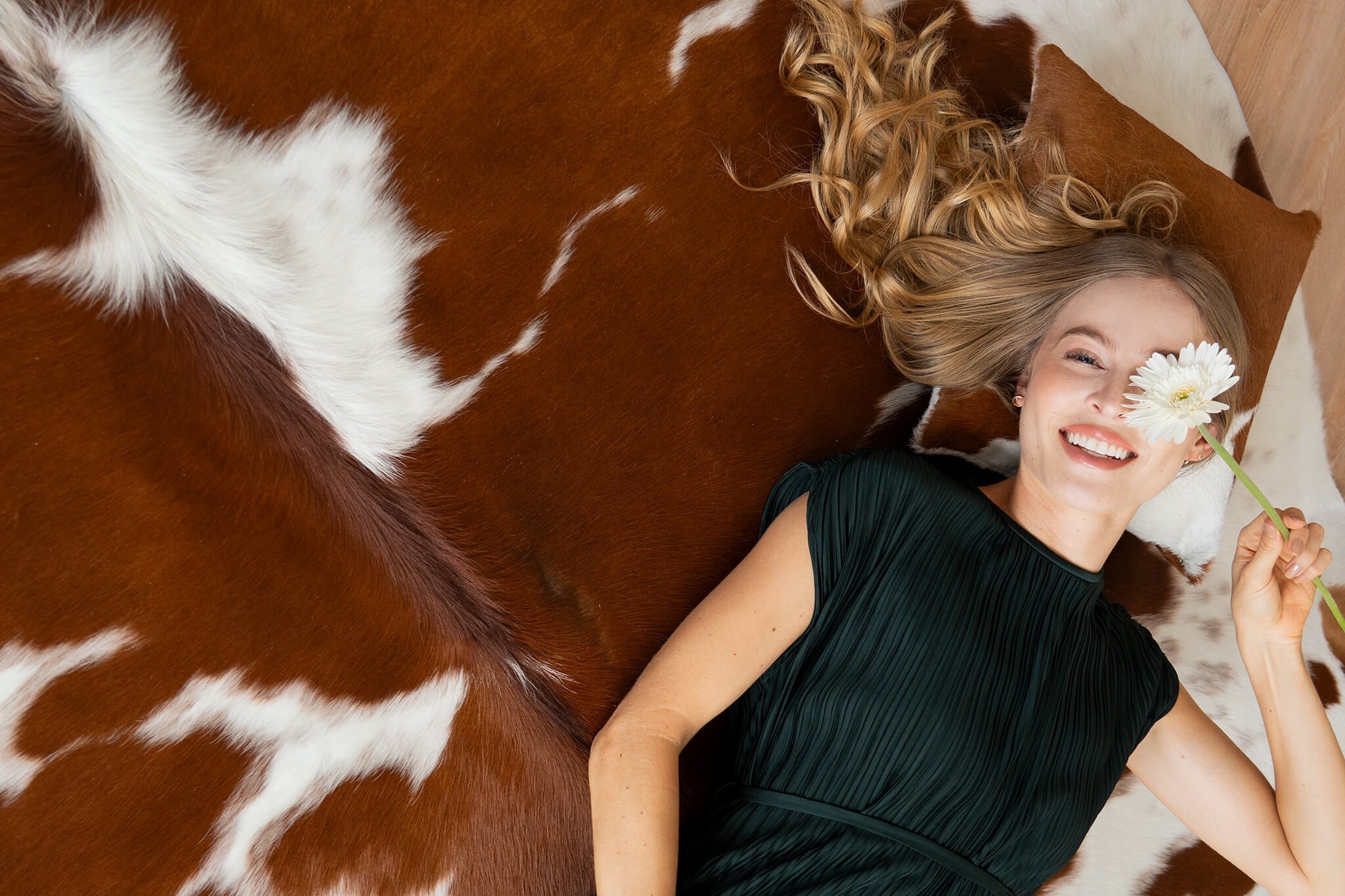Cowhide rug in a rich brown and white pattern, shown in a lifestyle overhead shot with a woman resting on the soft, natural hair-on-hide surface.
