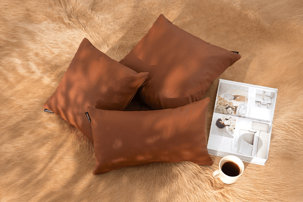Three brown throw pillows arranged on a tan faux-fur surface, with a small white tray and a cup of coffee nearby.