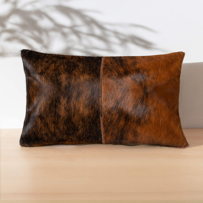 Brown cowhide pillow on a beige surface with a blurred plant in the background