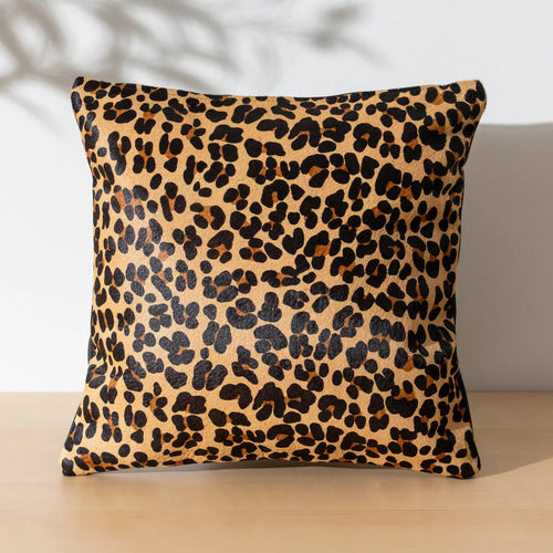Leopard print cowhide pillow on a wooden surface with a neutral background