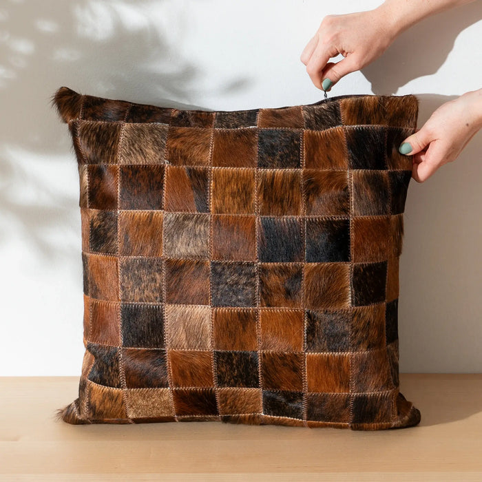 Patchwork pillow with brown and black squares held by a hand on a light background