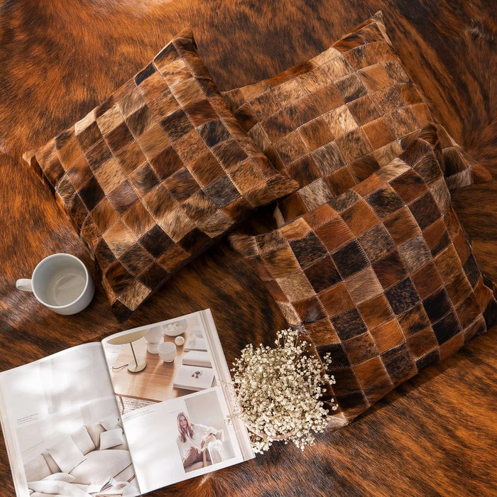 Brown checkered pillow on a textured surface with a magazine and flowers nearby