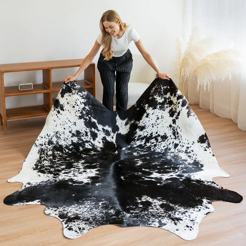 Woman unfolding a black and white salt and pepper cowhide rug on a wooden floor.