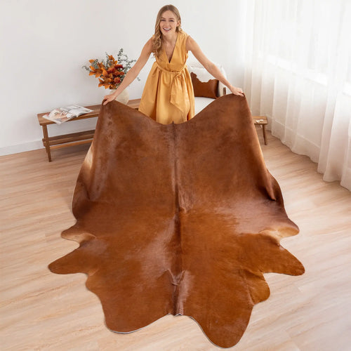 Woman holding a large brown cowhide rug in a room with wooden flooring and a small table.