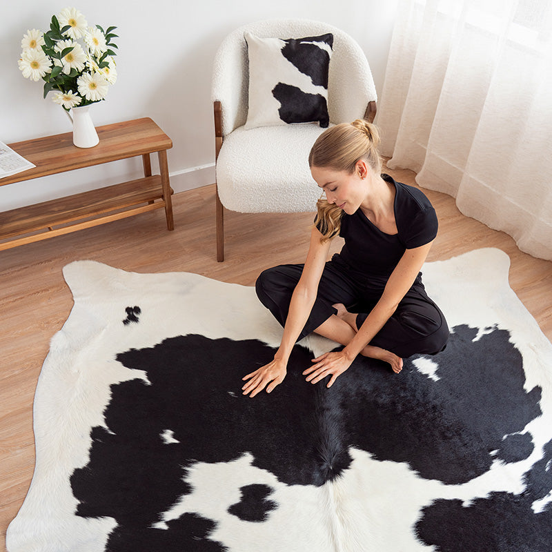 Woman sitting on a black and white cow hide rug in a room with a chair and table.
