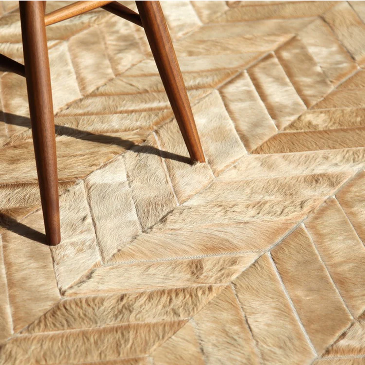 Close-up of a cowhide rug with a herringbone pattern and a wooden chair leg.