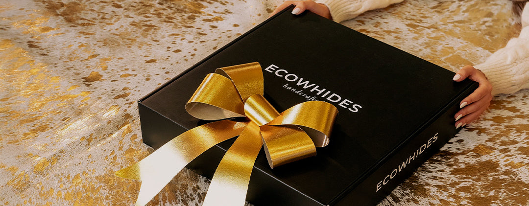 Black gift box with gold ribbon and 'ECOWHIDES' branding on a textured surface.